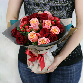 Яркий букет из красных и розовых роз с гиперикумом в упаковке